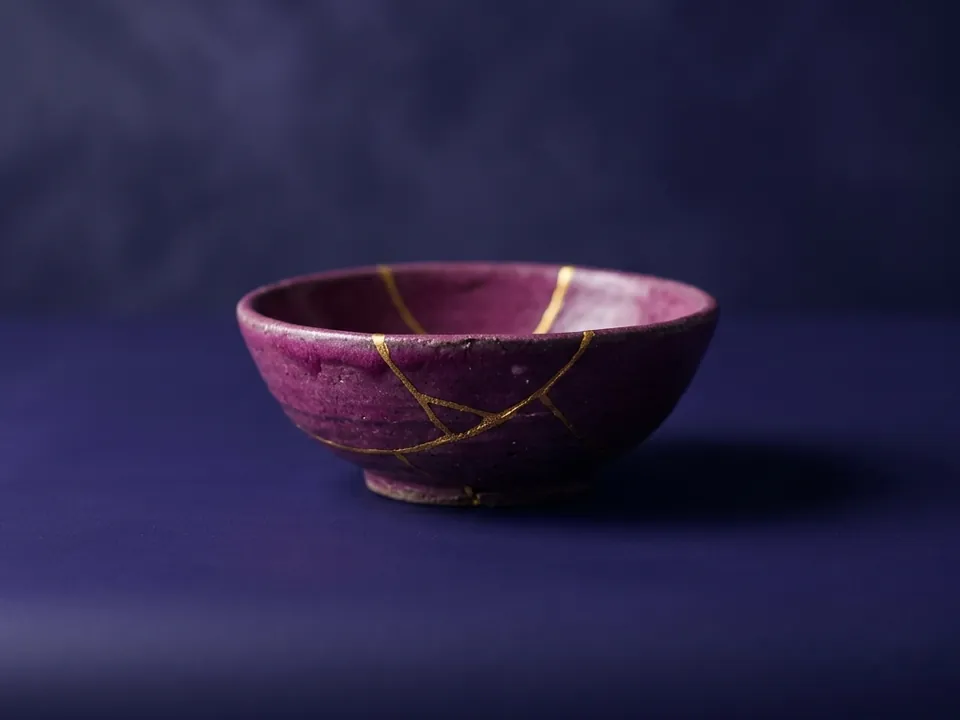 Cuenco de cerámica magenta reparado con vetas doradas al estilo kintsugi.