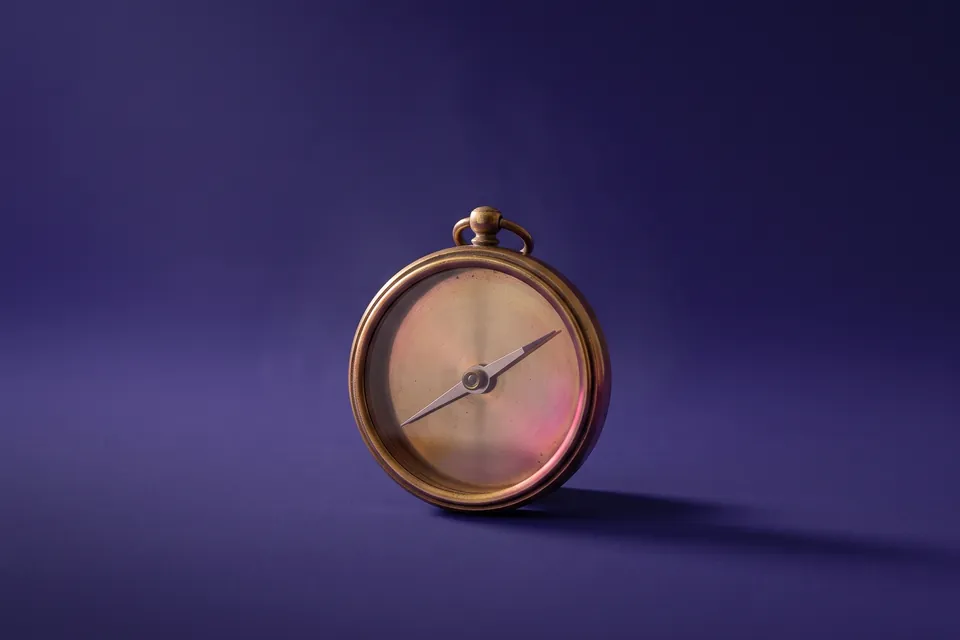 Brújula de bronce sin letras ni números, con solo la aguja, sobre fondo violeta.