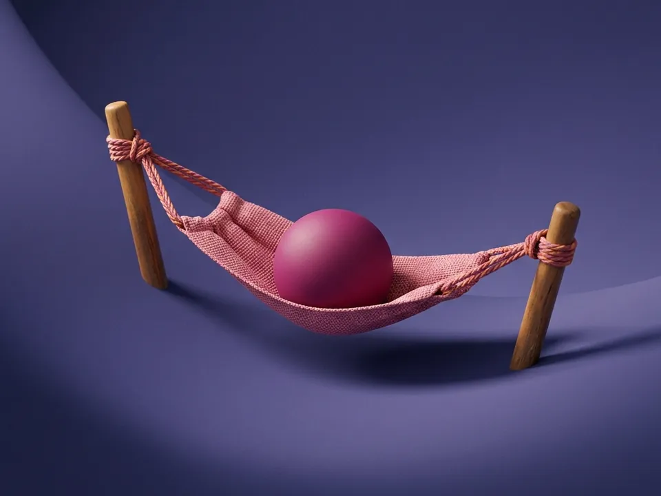 Pequeña hamaca de tela rosa tensada entre dos estacas de madera que sostiene una esfera magenta.