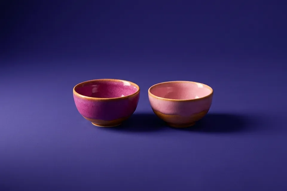 Dos cuencos de cerámica, uno magenta y otro rosa, uno al lado del otro sobre fondo violeta.